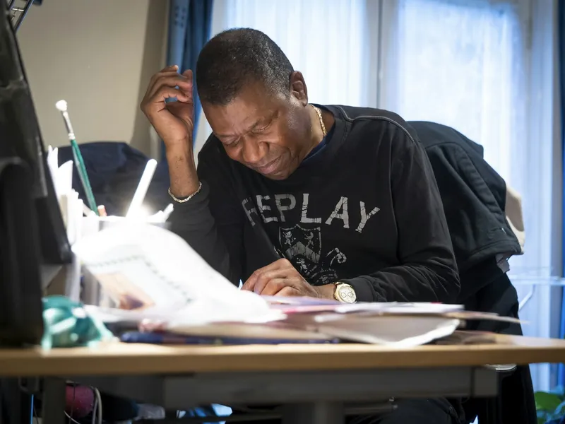 A man sits at a desk working through paperwork beside a computer.